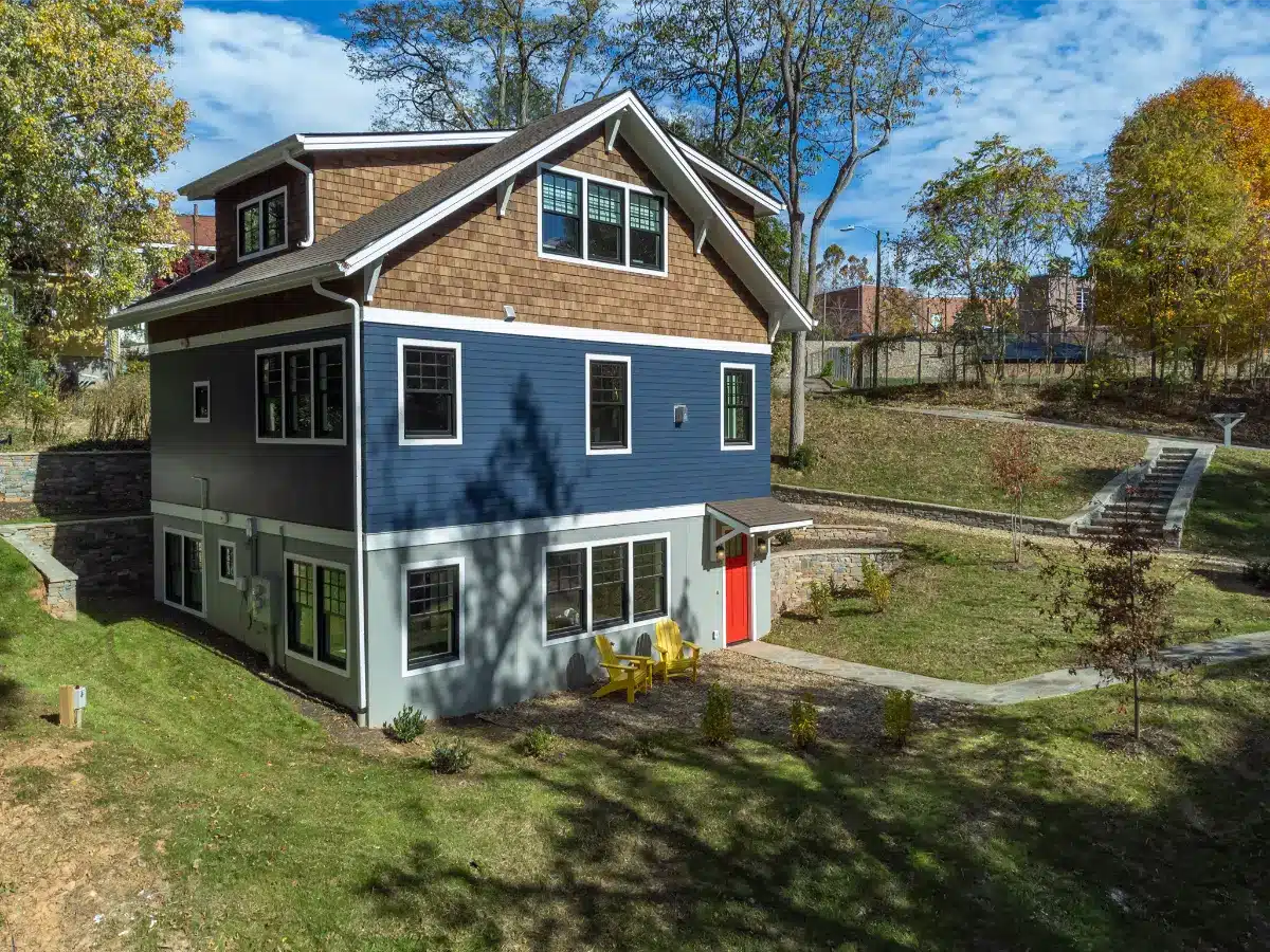Modern three-story ADU in Asheville, NC, featuring blue lap siding, natural wood shingles, and a bright red entrance door.
