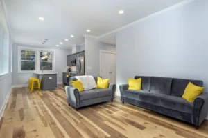 Open floor plan living space showcasing continuous natural hardwood flooring and modern grey sofas with yellow pillows.