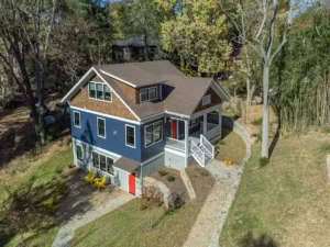 Custom craftsman-style house with blue siding, cedar shake gables, a bold red front door, and a stone paver walkway.