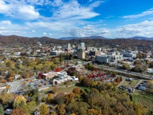 Scenic aerial drone view of a valley town nestled among rolling mountain hills and colorful autumn tree foliage.