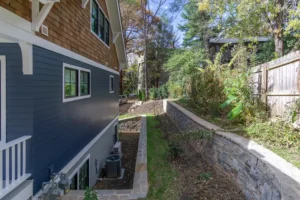 Side exterior view of a custom home highlighting blue siding and a concrete block retaining wall along a sloped lot.