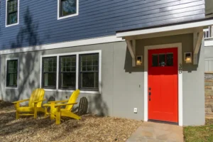 Outdoor seating area with bright yellow adirondack chairs next to a custom home's foundation and red door.