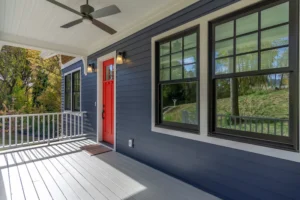 Covered front entry porch detail featuring dark blue siding, a white ceiling, and a vibrant red entry door.