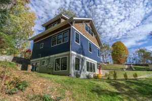 Low-angle view looking up a grassy hill at a modern custom home with blue horizontal siding.