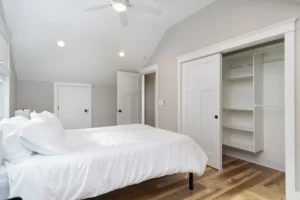 Bright, minimalist bedroom featuring clean white walls, a white bed, and a central ceiling fan.