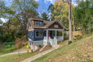 Full front elevation of a newly built blue craftsman home nestled among mature trees.