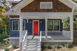 Close-up of a craftsman home front porch featuring white stairs, clean railings, and a bold red front door.