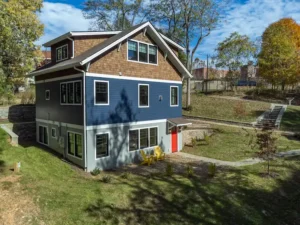 Distant exterior view of a custom two-story blue house situated on a green, sloped yard.