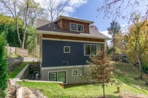 Side perspective of a blue-sided house showing windows and a clean foundation on a grassy slope.