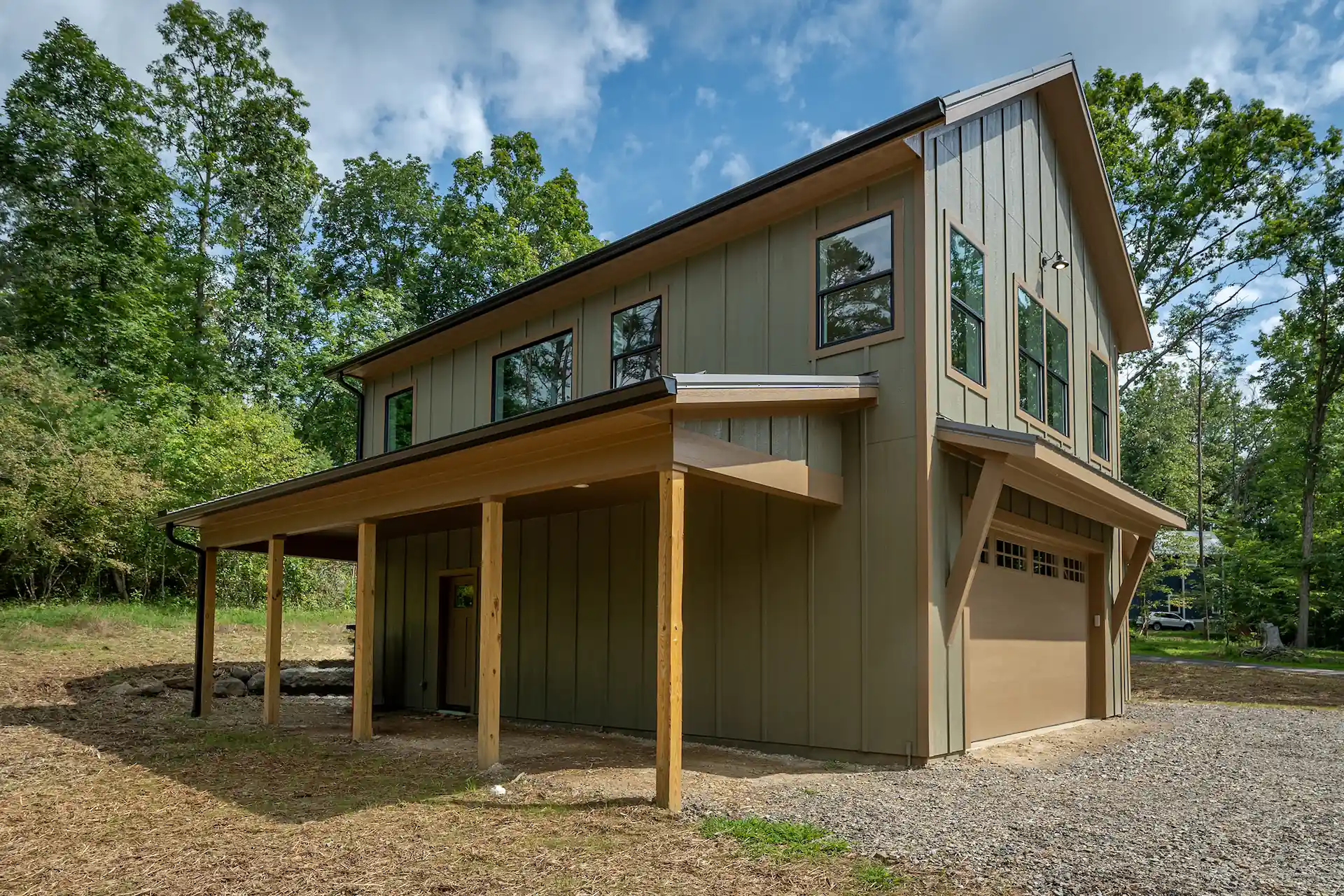Two-story detached garage apartment with green vertical board and batten siding, a wide covered front porch with natural wood posts, and a dark metal roof.
