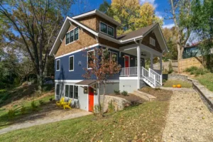 Angle exterior view of a custom three-story craftsman home featuring dark blue siding, cedar shake gables, and a stone foundation.