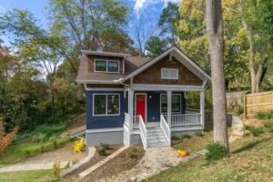 Complete front exterior of a two-story craftsman house with blue siding, natural cedar shake gables, a white porch, and a red door.