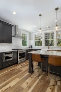 Modern kitchen design highlighting dark grey shaker-style cabinets, a large white island countertop, and custom leather barstools.