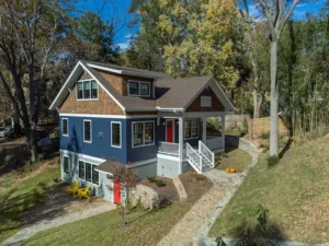 Full front elevation of a completed custom craftsman home built on a sloped lot with a stone paver walkway.
