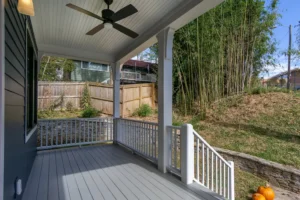 Covered outdoor living space on a painted grey wooden deck with clean white railings looking out toward trees.