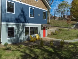 Corner exterior view of a custom two-story blue craftsman house highlighting a striking red front door and a stone foundation.
