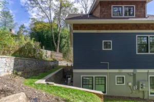 Close-up side exterior of a custom blue home showing a concrete block retaining wall stabilizing a sloped lot.