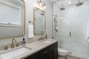 Contemporary bathroom featuring a dark vanity with a stone countertop, a gold-rimmed mirror, and a white subway tile walk-in shower.