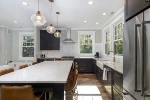 Modern kitchen layout with dark cabinetry, premium white countertops, glass pendant lights, and a white subway tile backsplash.