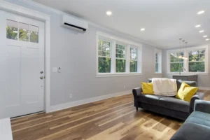 Bright empty interior room showcasing rich natural hardwood floors, light grey walls, and large windows.