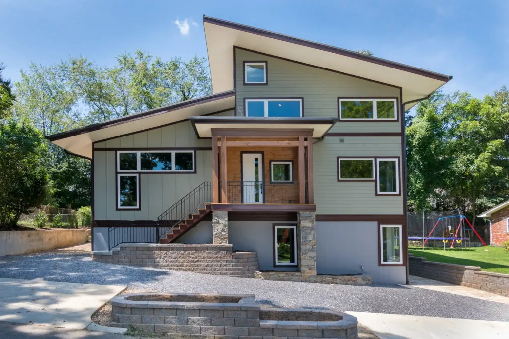 Architectural exterior view of a custom multi-level home with green and beige siding, large windows, and stone foundation accents.