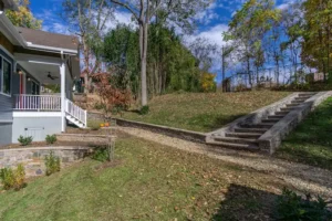 Landscaped sloped yard featuring a stone block retaining wall with integrated steps and a green grass lawn.