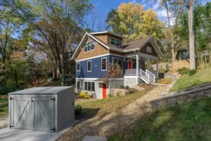 Exterior side perspective of a blue craftsman house built on a sloped lot with a stone veneer foundation.