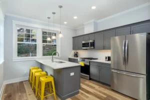 Contemporary kitchen design with dark gray shaker cabinets, stainless steel appliances, quartz countertops, and yellow barstools.