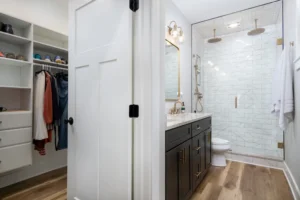 Bathroom view looking through a doorway showing a dark wood vanity and a clean white subway-tile walk-in shower.